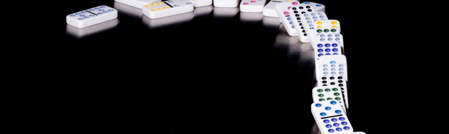 Dominoes falling in a curved line on a dark surface