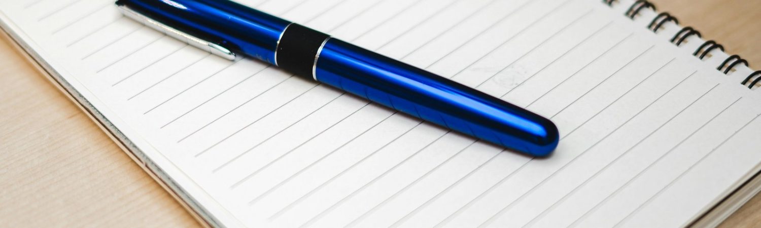 A blue pen resting on a lined notebook