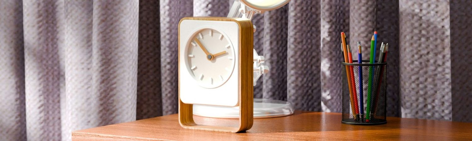 A desk clock beside pens on a wooden desk
